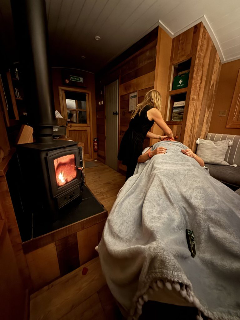 Massage treatment beside a lit log burner inside a shepherd's hut at Ockeridge Rural Retreats