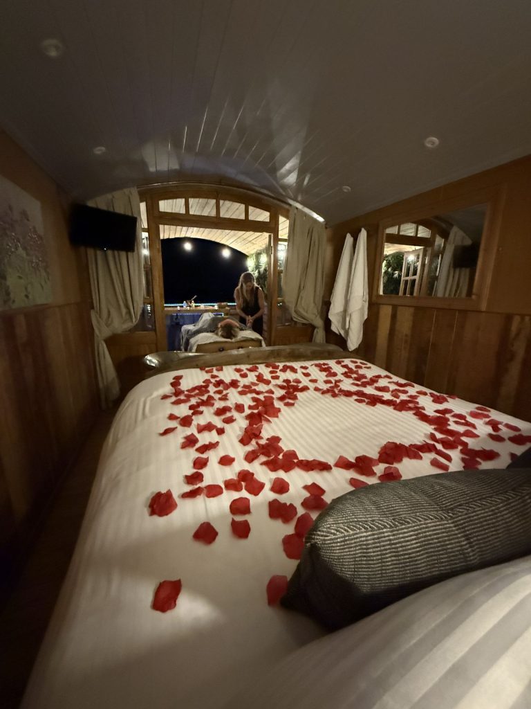 Rose petal heart on the bed of a shepherd's hut with a treatment taking place beyond, Ockeridge Rural Retreats