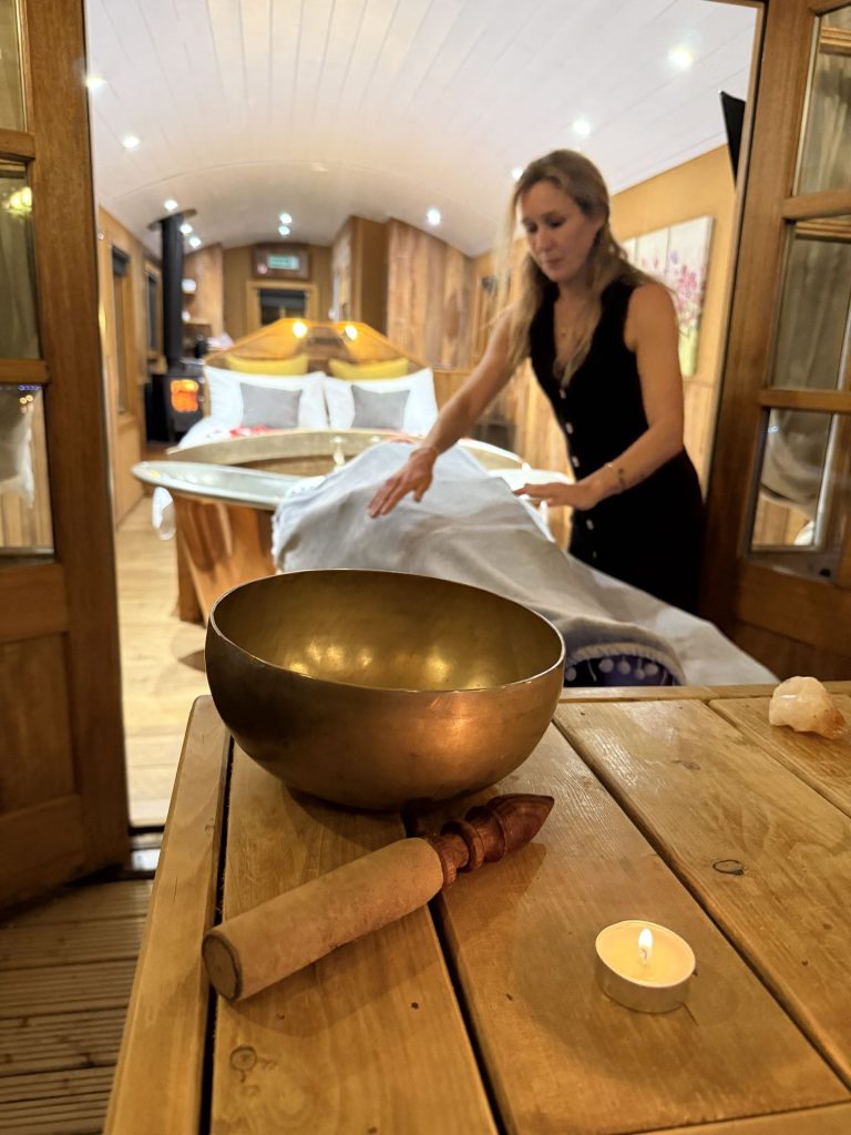 Brass singing bowl, candle and crystals on the decking with a massage couch behind, shepherd's hut treatment at Ockeridge